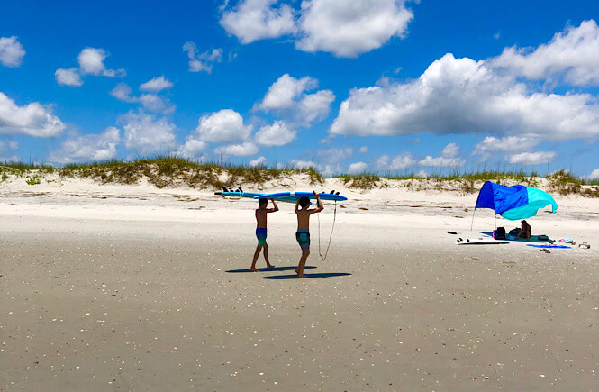 The ultimate list of what to bring to the beach featured by top US travel blog, More than Main Street: image of boys surfing on beach in NC.