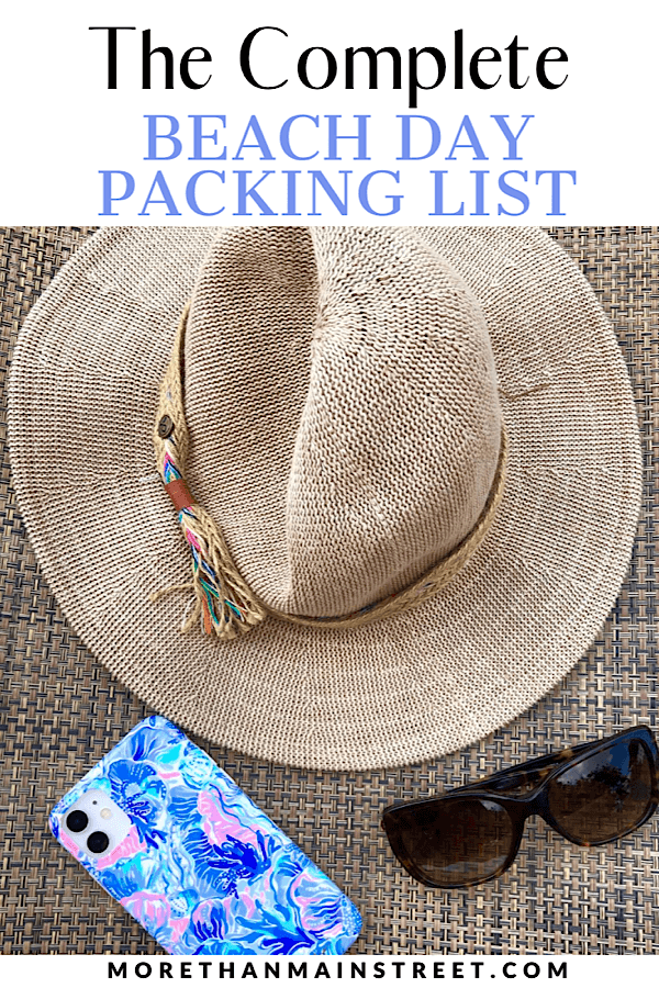 The ultimate list of what to bring to the beach featured by top US travel blog, More than Main Street: flat lay of beach hat, phone, and sunglasses.