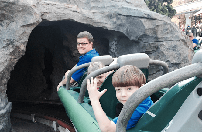 One of the most fun day trips from San Diego with kids is of course Disneyland!! Image of a Dad and two kids on a ride at Disneyland.