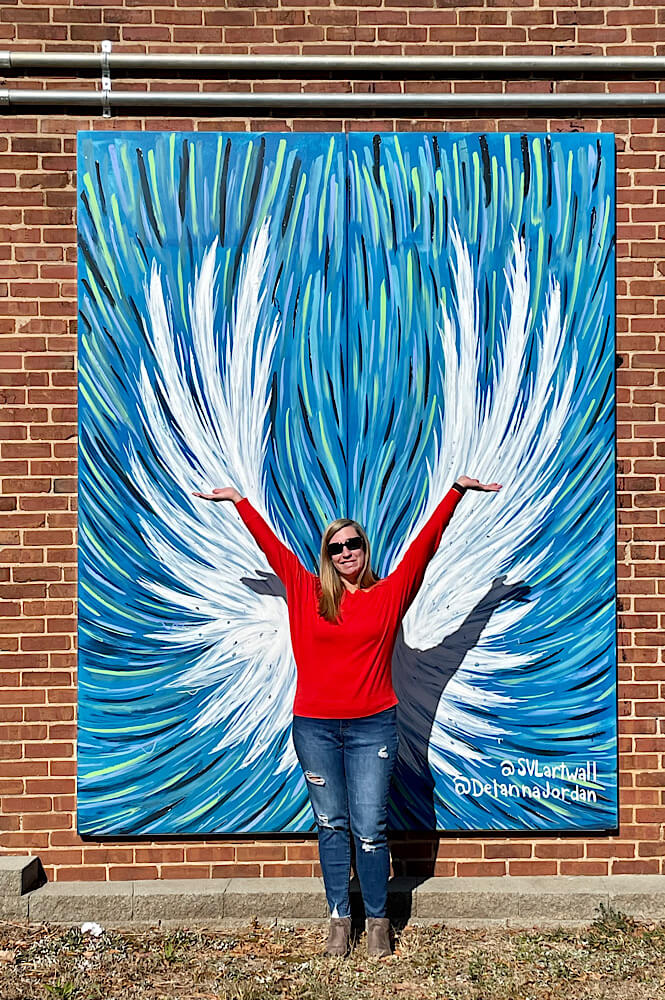 Girl in a red shirt standing in front of white and blue feathered wings at the Statesville NC art wall.