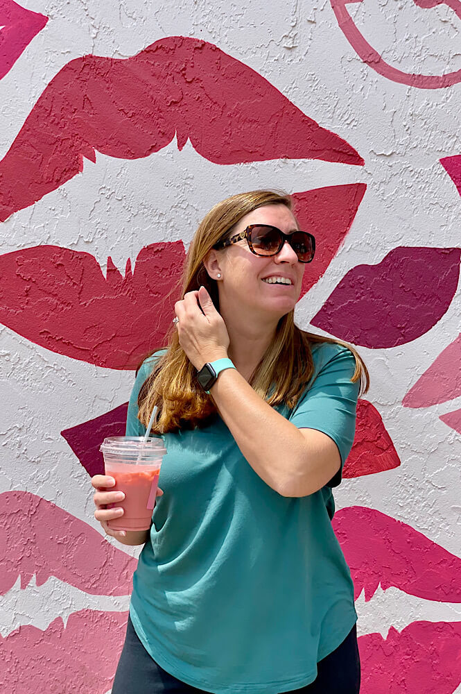 girl in front of a wall mural of pink lips holding a pink coffee from Spill Coffee in Wilmington NC