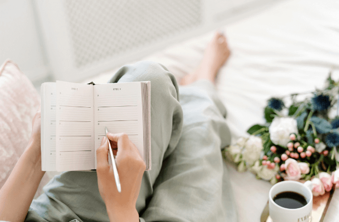 woman lounging while writing in a journal with a cup of coffee by her side