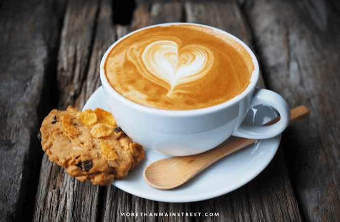 latte with heart shaped latte art and a cookie on a saucer