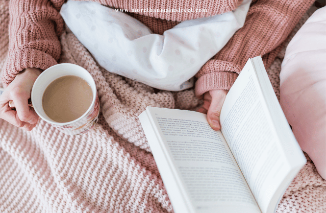 woman holding a book and coffee in bed in pink tones