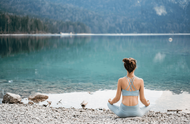 a woman practicing yoga by a lake