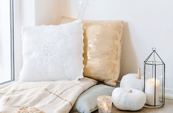 self care sundays: image of two pillows, candles, and a blanket in a cozy corner
