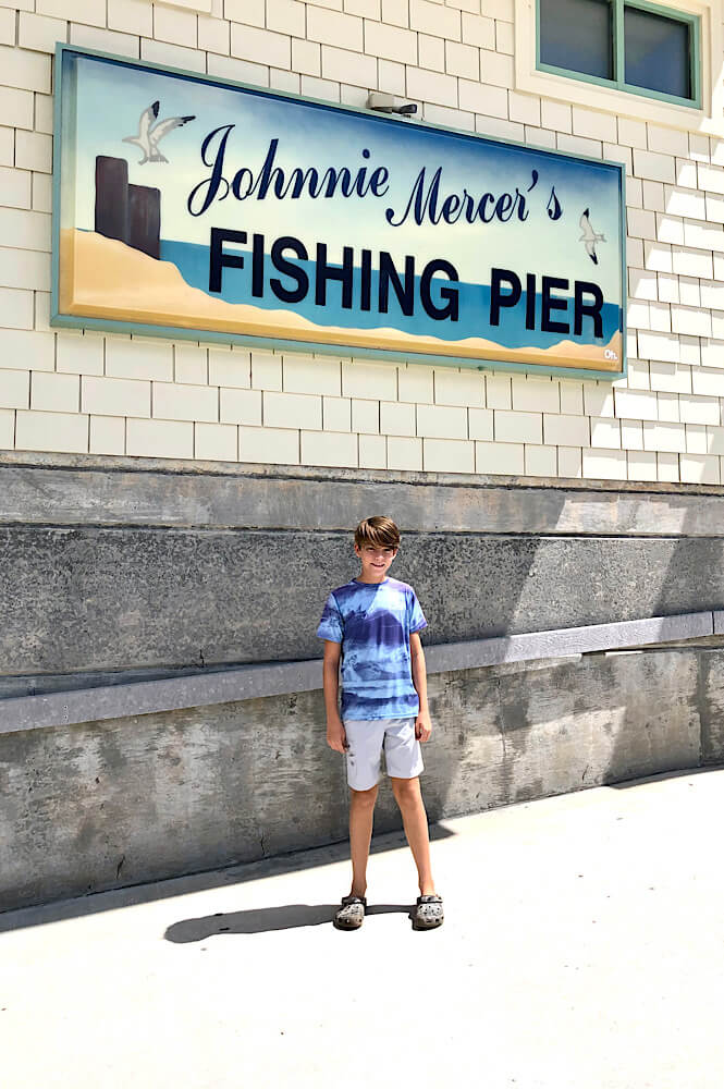 Boy standing in front of Johnny Mercer's Fishing Pier sign in Wrightsville Beach