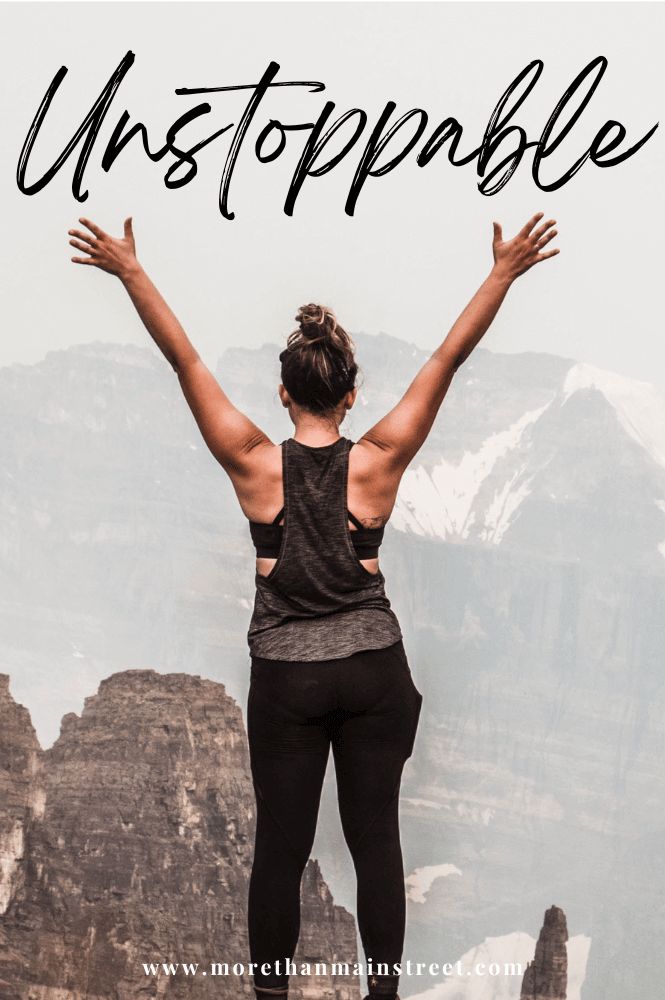 Woman on a mountain top with arms in the air and caption says unstoppable
