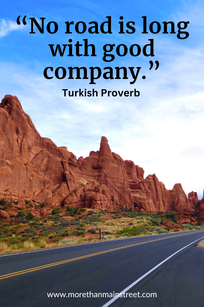 Road in Arches National Park with road trip quote "No road is long with good company."