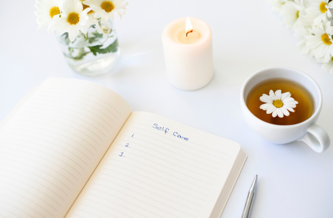 image of a journal with a blank list for self care, tea, a candle and flowers