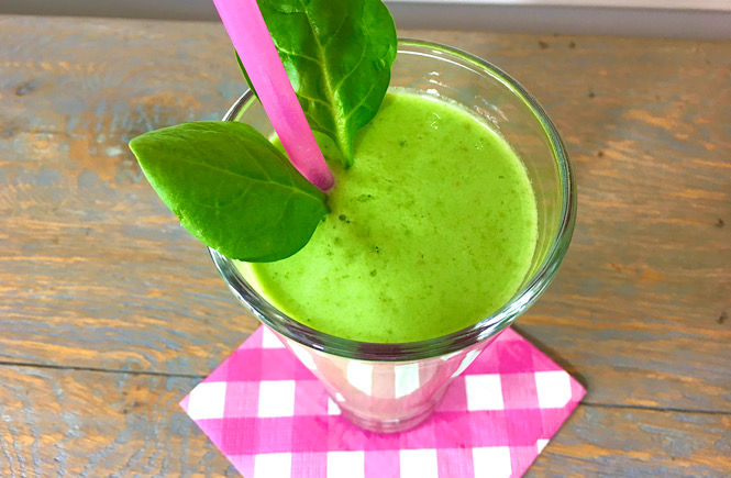 Homemade green smoothie with a fun pink napkin and straw and a little green spinach garnish showing how you can make your food a little fancy and fun even at home.