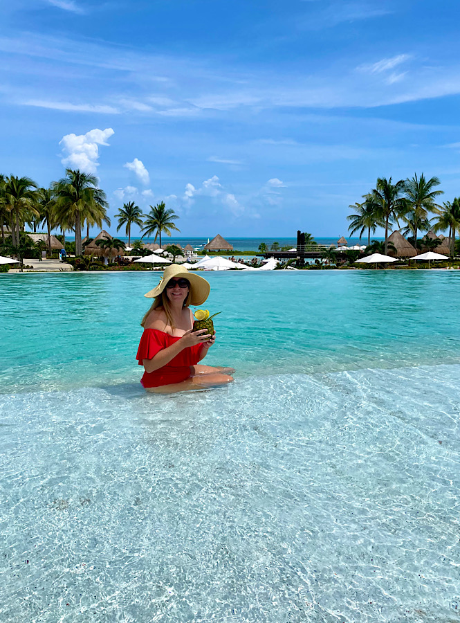 woman sitting in a pool with a red bathing suit and a pineapple drink at an all inclusive resort in Cancun Mexico