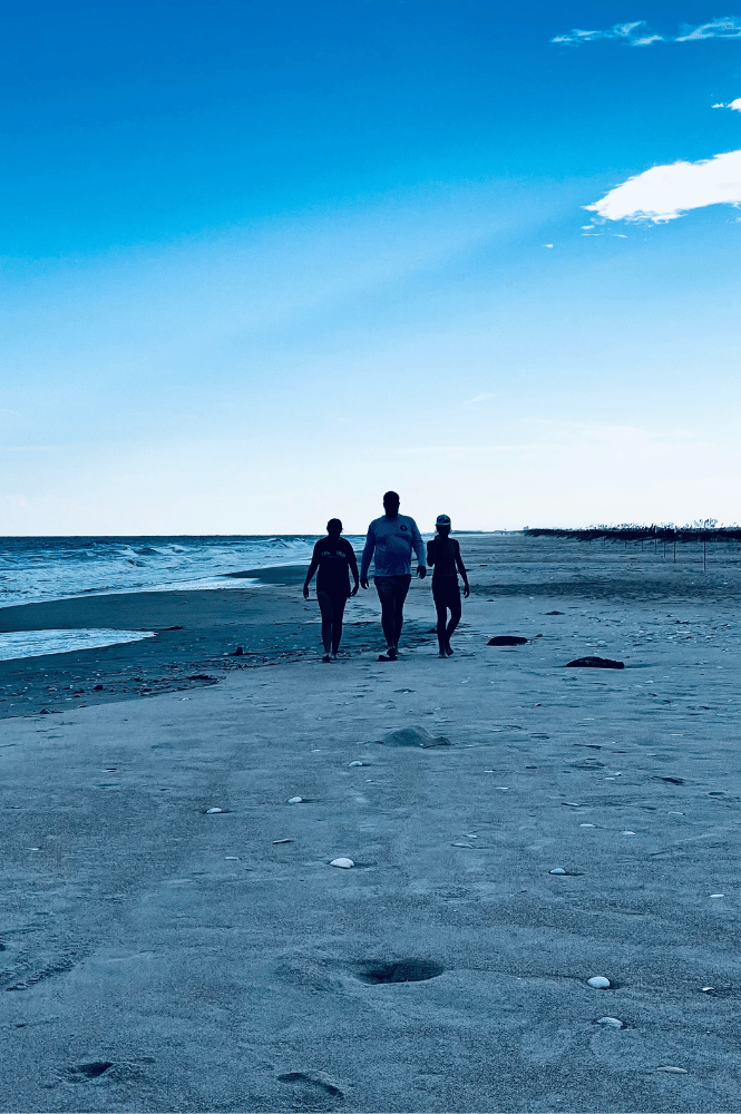 A photo of father and kids silhouette walking towards the camera on a beach showing a memorable travel moment worth documenting in a travel journal.