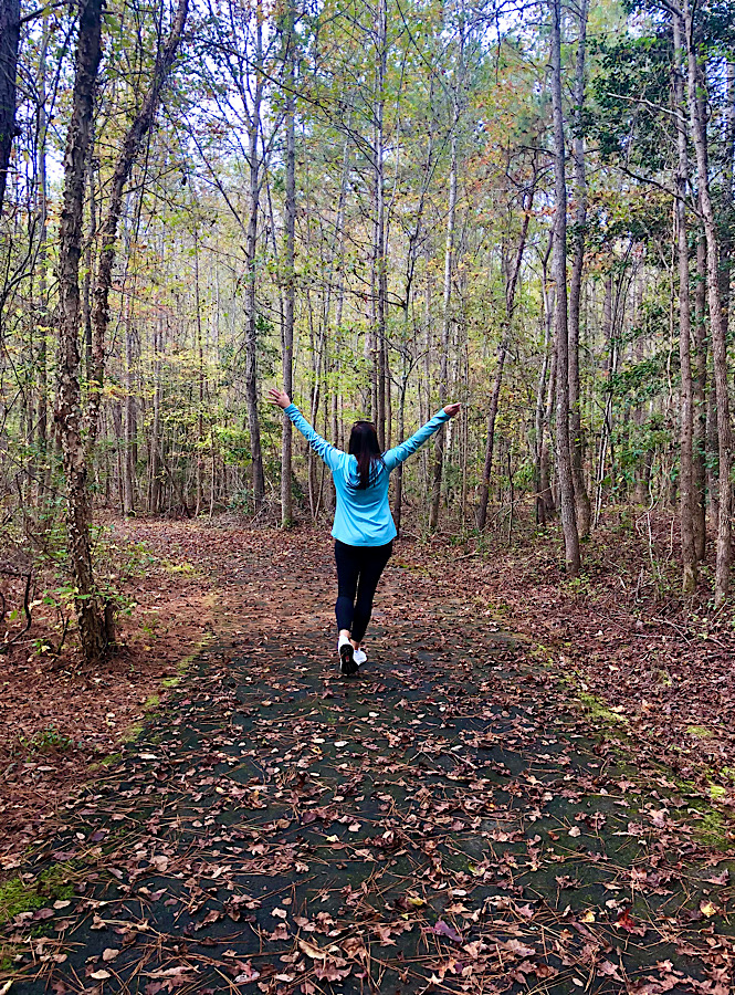 Woman with her hands up walking a path in the woods embracing the fall weather.