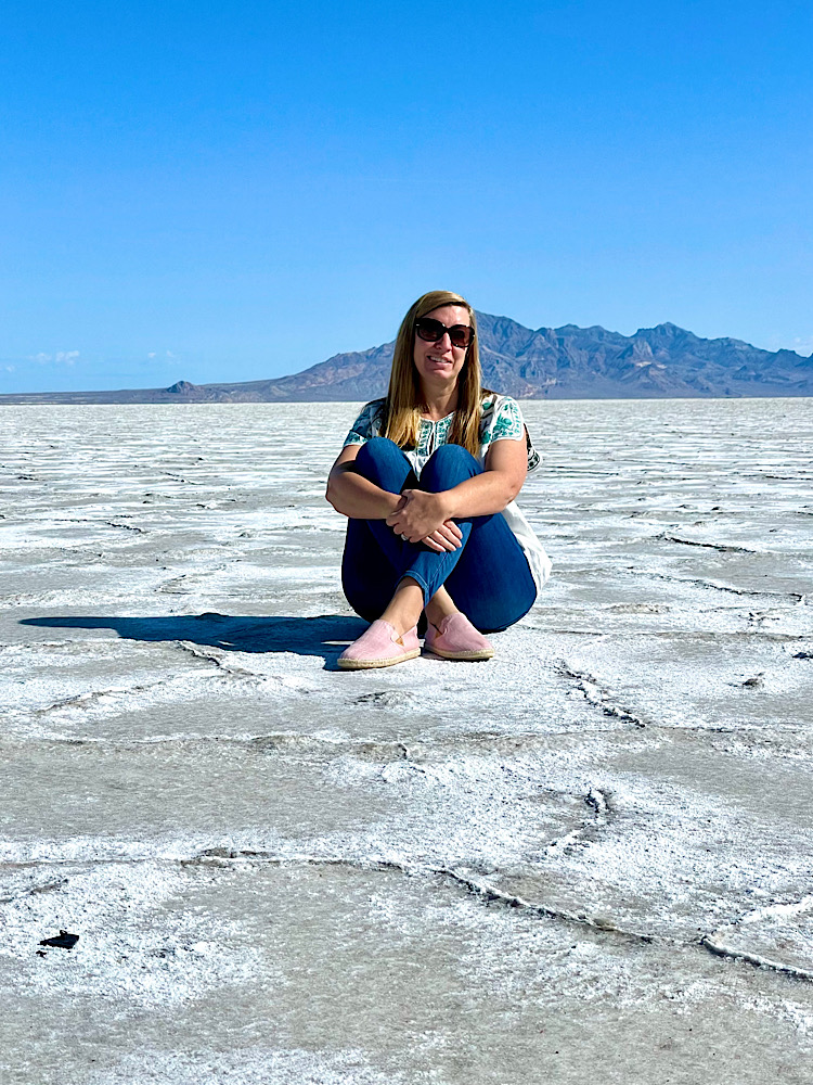 woman sitting crossed legs on the salt flats in Utah with a blue sky and mountains behind her feeling encouraged